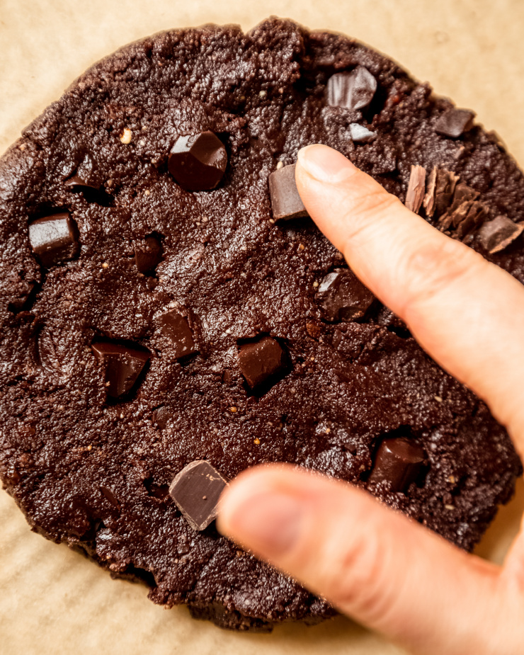 An up close, overhead image shows a finger pushing a chocolate chunk into a raw portion of cookie dough.