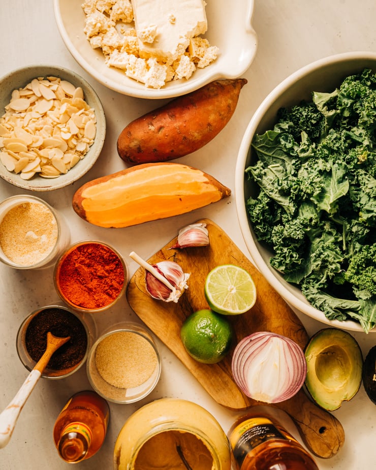 An overhead shot of ingredients used in a vegan kale power salad, featuring sweet potatoes, tofu, and avocado among other ingredients.