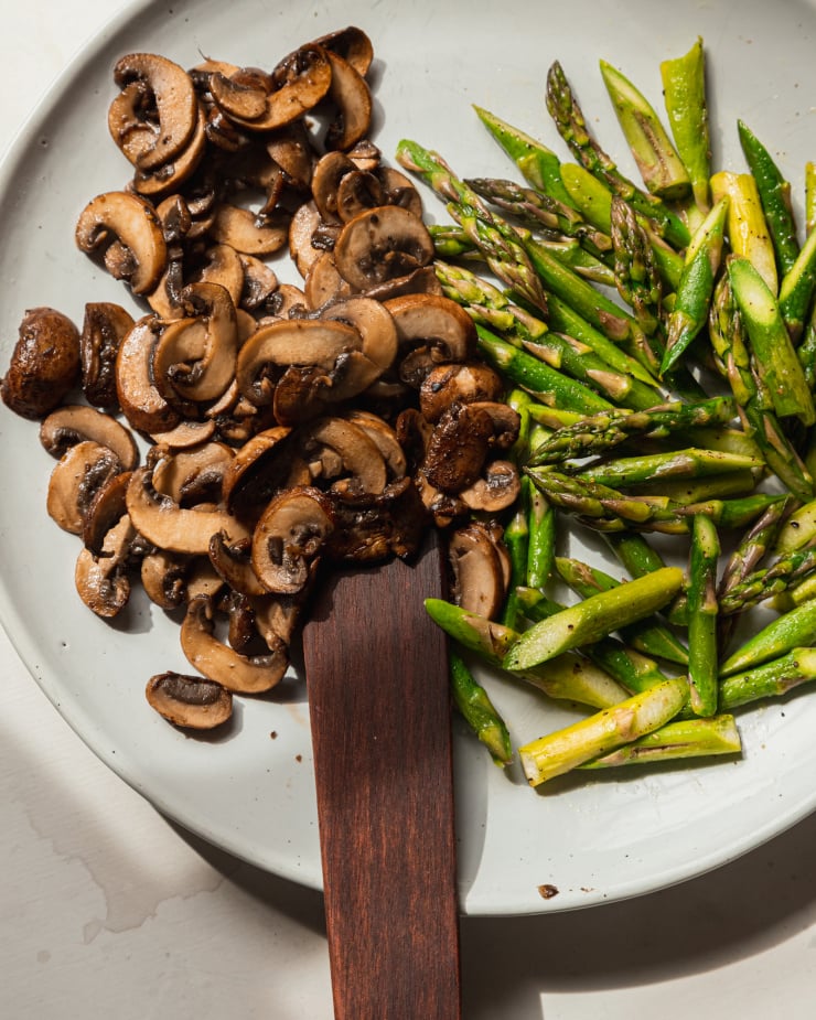 An overhead image shows sautéed mushrooms and asparagus on a very light blue/white plate.