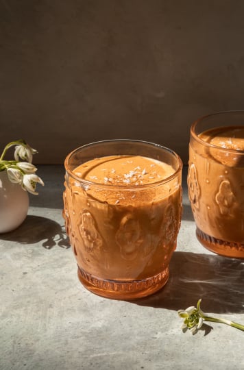 A head on shot of a light orange spring thaw smoothie in two glasses with a small vase of snow drop flowers in the background.