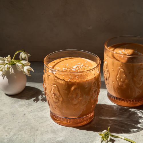 A head on shot of a light orange spring thaw smoothie in two glasses with a small vase of snow drop flowers in the background.