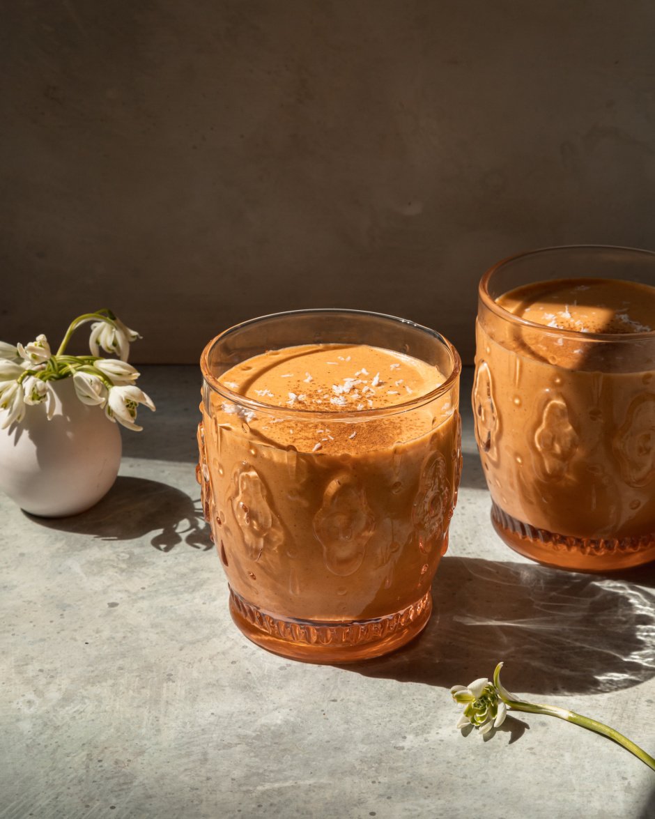 A head on shot of a light orange spring thaw smoothie in two glasses with a small vase of snow drop flowers in the background.