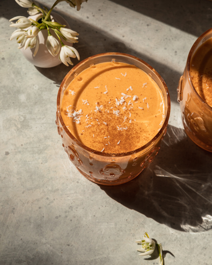 An overhead image shows a light orange smoothie in a glass, garnsihed with ground cinnamon and shredded coconut.
