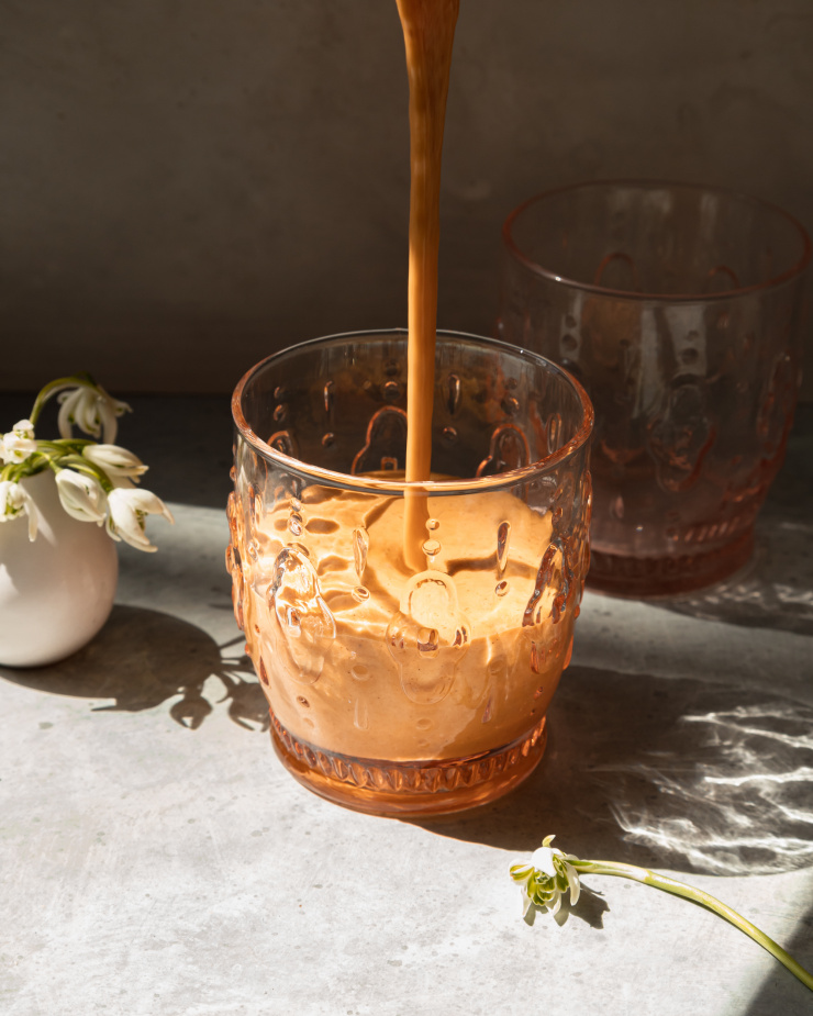 A head-on image shows a light orange smoothie being poured into an etched, clear glass.