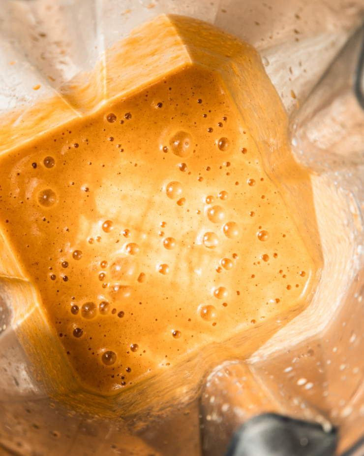 An up close, overhead shot of a blended light orange smoothie in a blender pitcher.