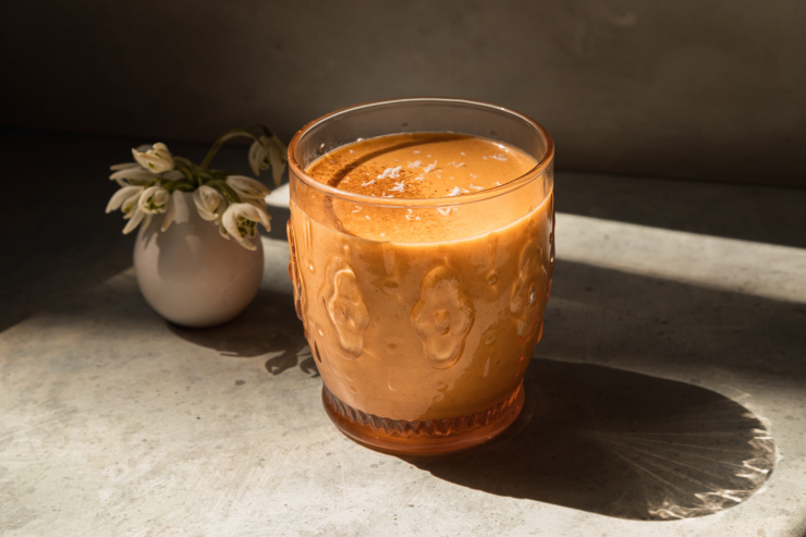 A head on shot of a light orange spring thaw smoothie with a small vase of snow drop flowers in the background.