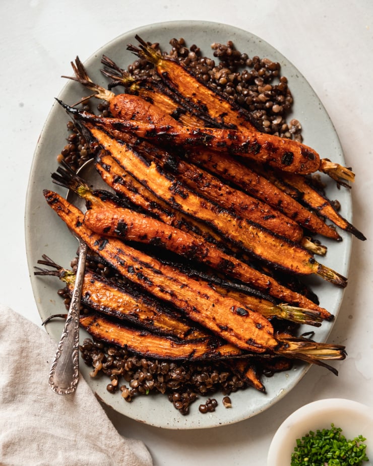 Overhead image shows grilled carrots on top of a bed of lentils, on a pale blue oval plate.
