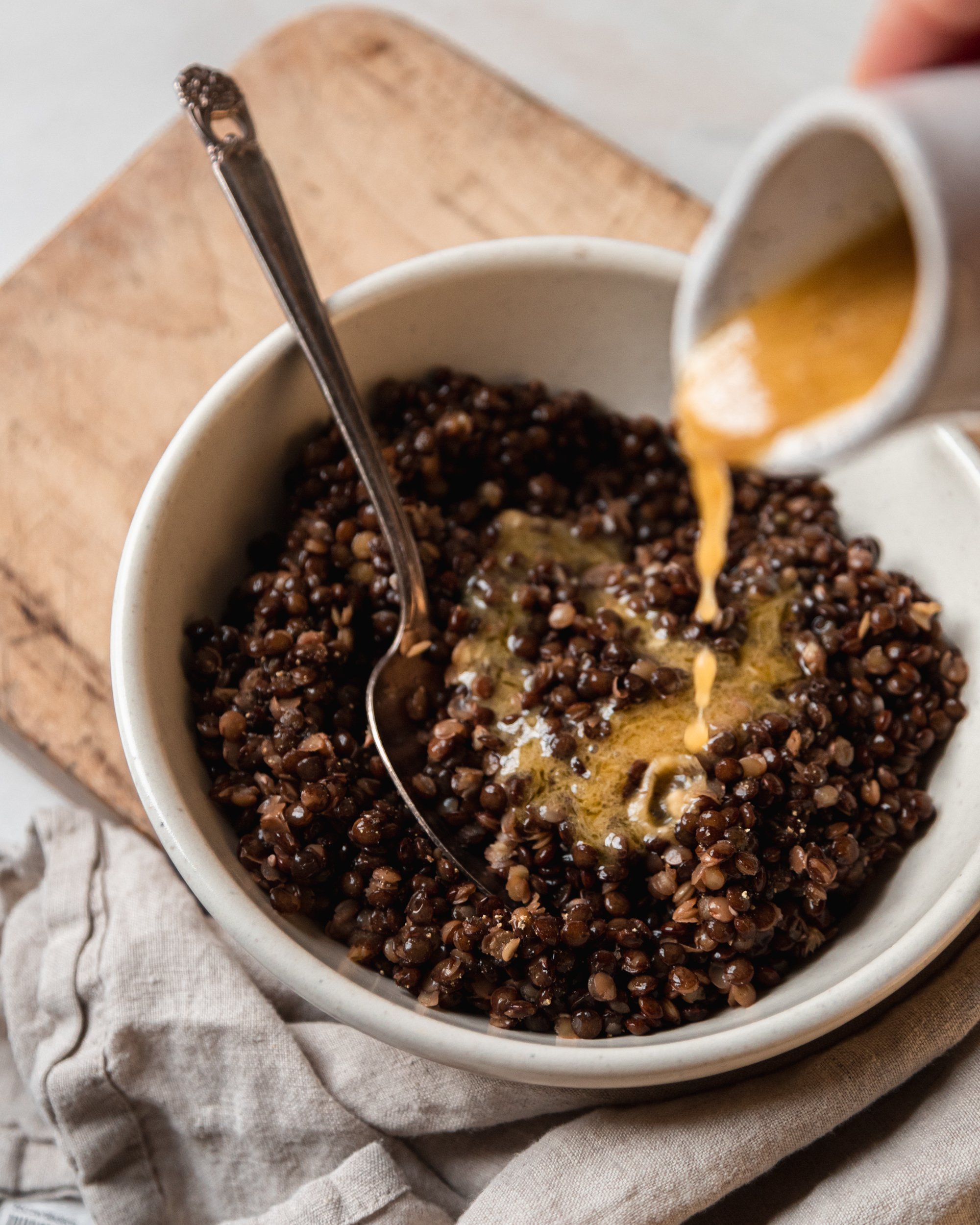 Overhead image shows vinaigrette being poured into a bowl of cooked French lentils.
