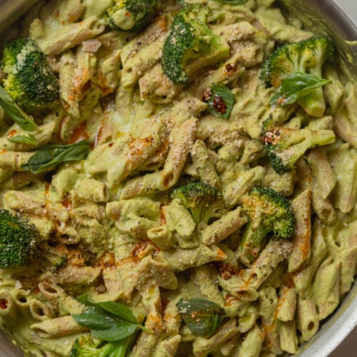 An up close, overhead shot of a creamy green-sauced pasta with broccoli florets and drizzles of deep red chili oil. The 30 minute broccoli basil pasta is shown in a large stainless steel sauté pan.