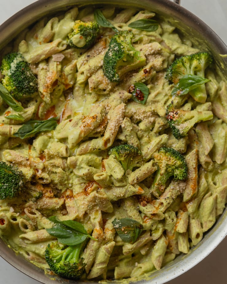 An up close, overhead shot of a creamy green-sauced pasta with broccoli florets and drizzles of deep red chili oil. The 30 minute broccoli basil pasta is shown in a large stainless steel sauté pan.