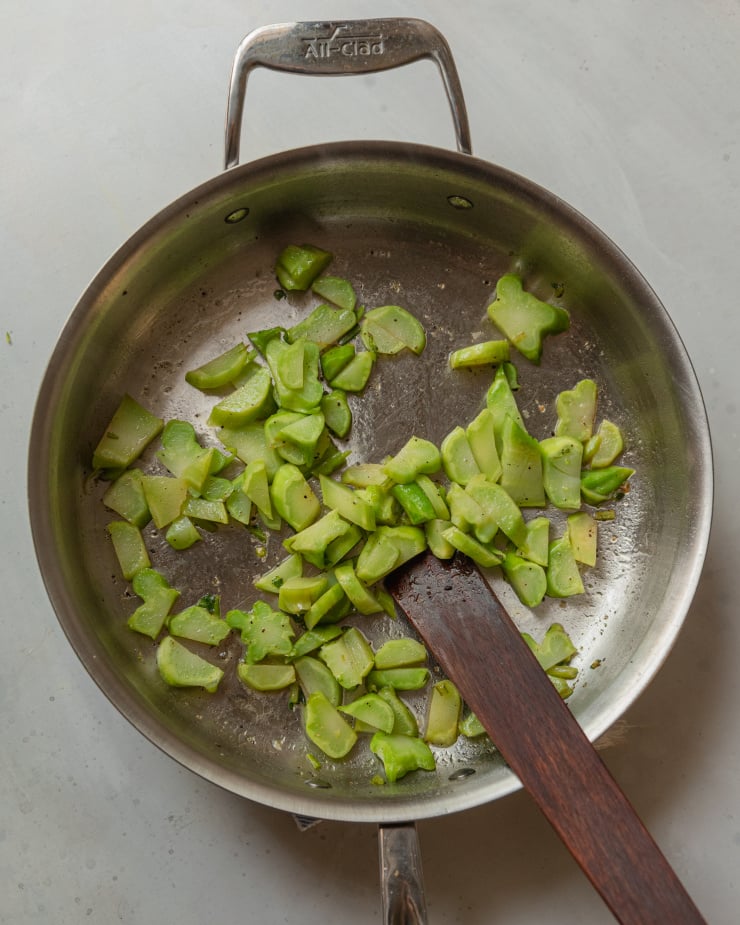 An overhead shot of broccoli stems being sautéed in a stainless steel sauté pan.
