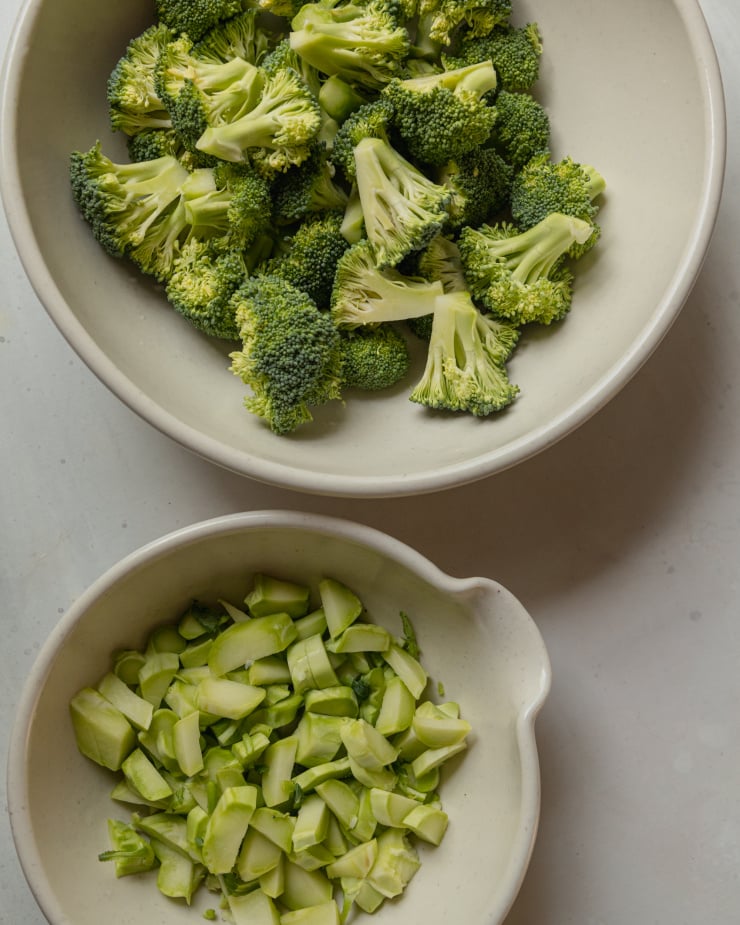 An overhead shot showing broccoli florets in one bowl and chopped up broccoli stems in another, smaller bowl.