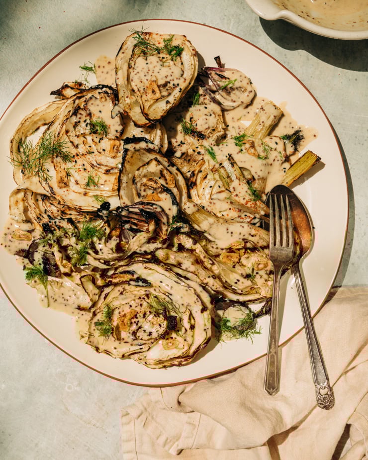 An overhead shot of grilled cabbage and fennel in direct sunlight. The vegetables are covered in a creamy mustard seed sauce and garnished with fennel fronds.