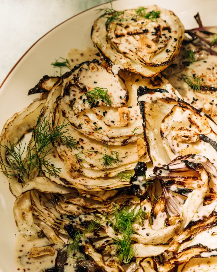 An up close, overhead shot of grilled cabbage and fennel in direct sunlight. The vegetables are covered in a creamy mustard seed sauce and garnished with fennel fronds.