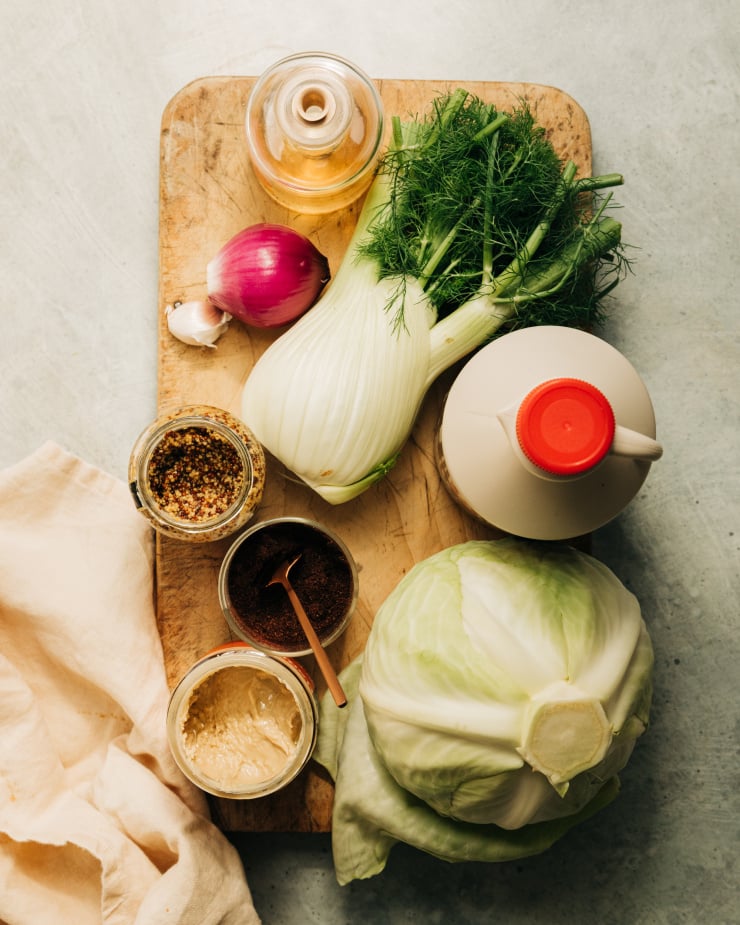 Overhead image shows ingredients for a grilled cabbage and fennel dish that is served with a vegan maple mustard cream.
