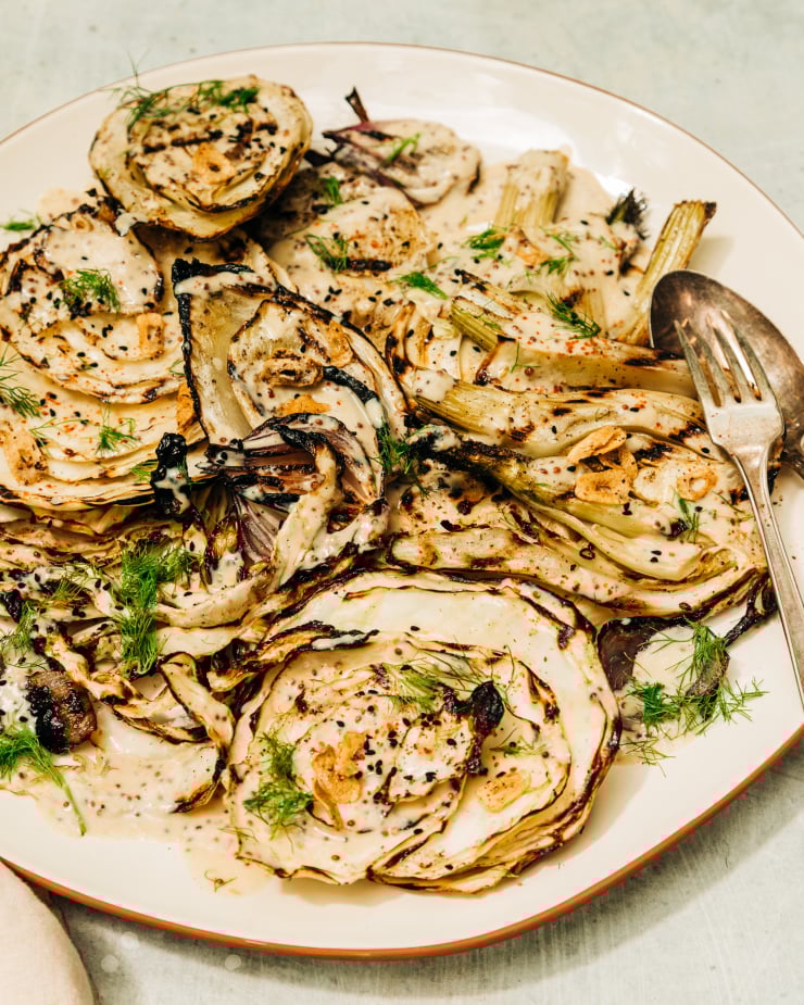 A 3/4 angle shot of grilled cabbage and fennel in direct sunlight. The vegetables are covered in a creamy mustard seed sauce and garnished with fennel fronds.