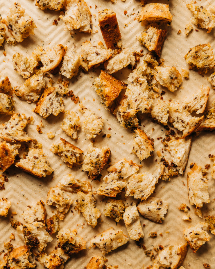 An up close, overhead shot of crispy, toasted ripped pieces of bread on a parchment-lined baking sheet.