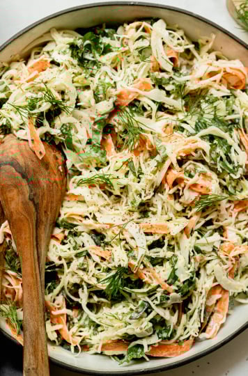 An up close, overhead shot of a cabbage, kale, and carrot slaw with creamy mustard dressing. The slaw is in a wide ceramic dish with a black rim.