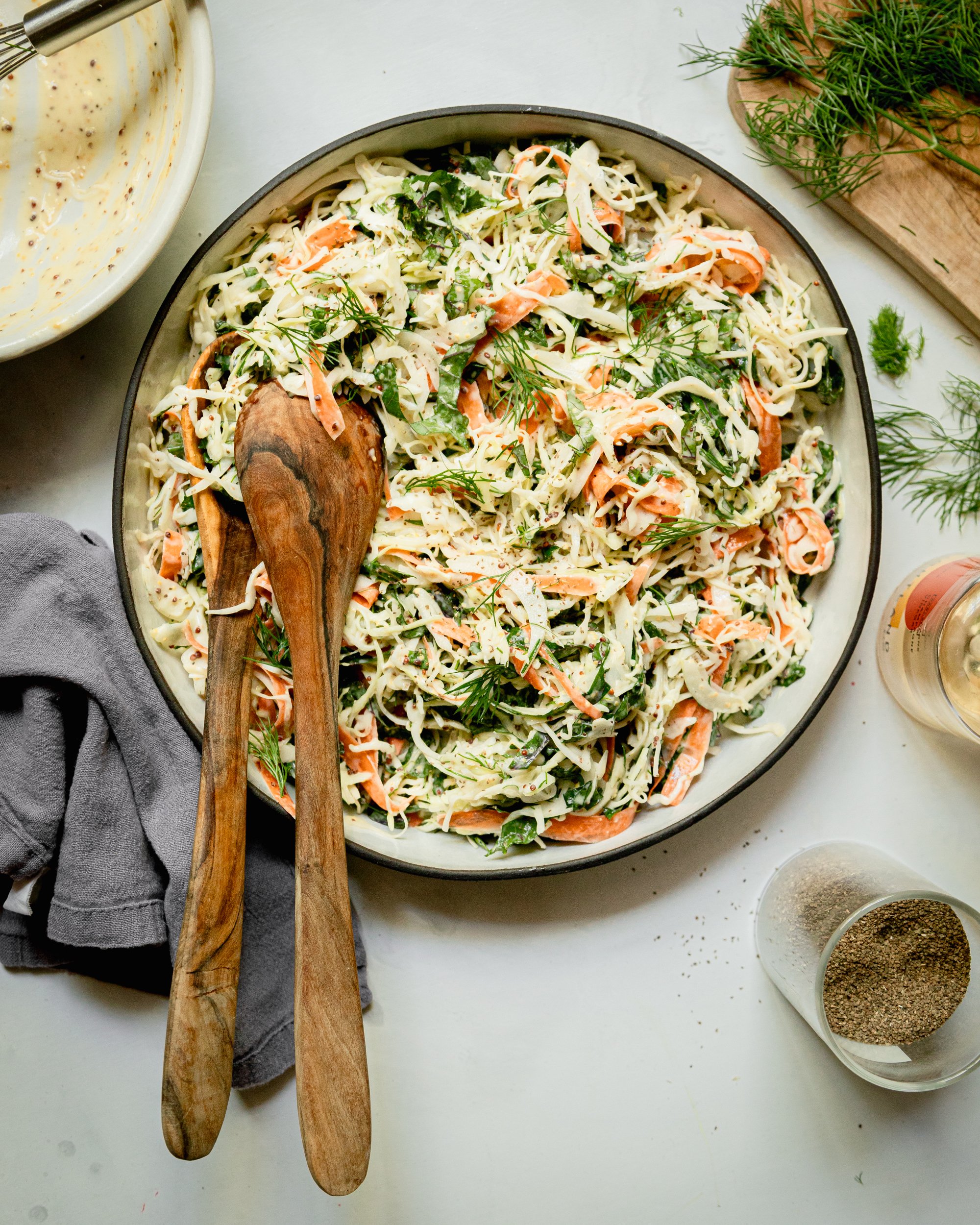An overhead shot of a cabbage, kale, and carrot slaw with creamy mustard dressing. The slaw is in a wide ceramic dish with a black rim.