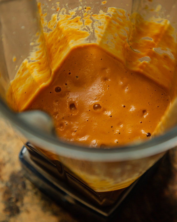 A 3/4 angle shot shows a creamy red pepper sauce in a blender pitcher. The sauce is pale orange.