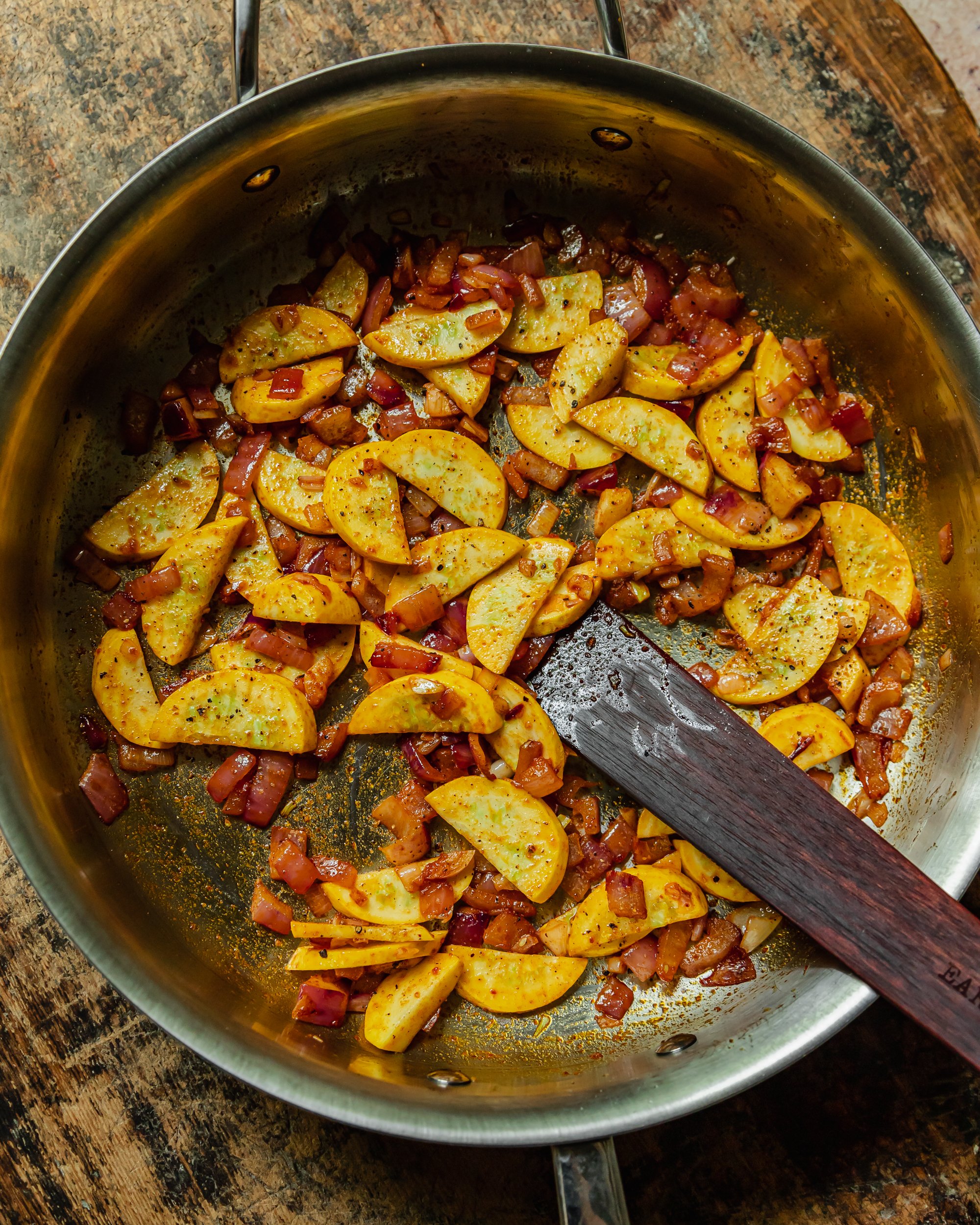 An overhead image shows slices of zucchini and red onion being sautéed with spices in a wide stainless steel pan.