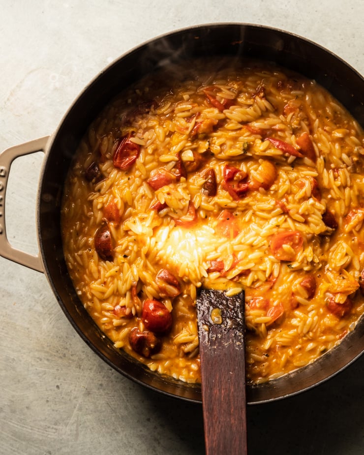 An overhead shot of a creamy vegan tomato orzo dish in a beige braiser-style pot.