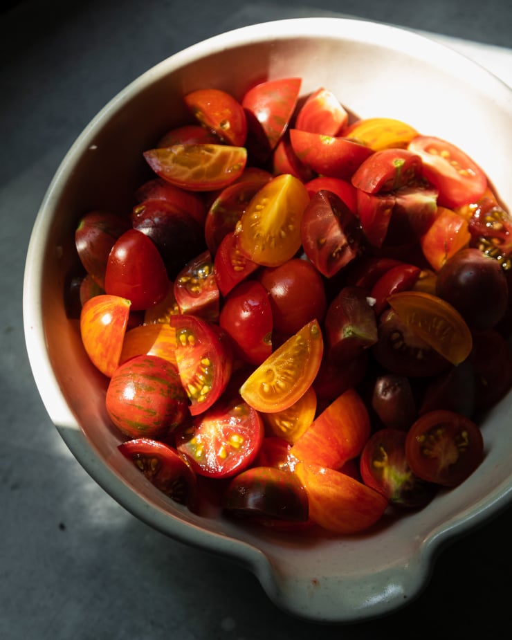 A slightly angled overhead shot shows chopped small tomatoes in a beige ceramic bowl.