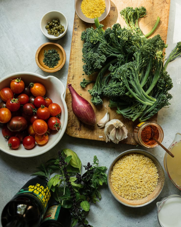 An overhead shot of ingredients used in a vegan tomato orzo dish with broccolini.