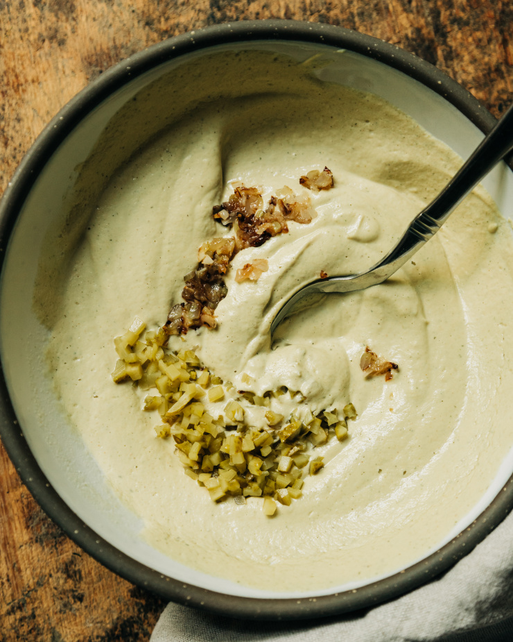 An overhead shot shows a creamy beige dip in a bowl with some finely minced sautéed onions and pickles on top, waiting to be stirred in.