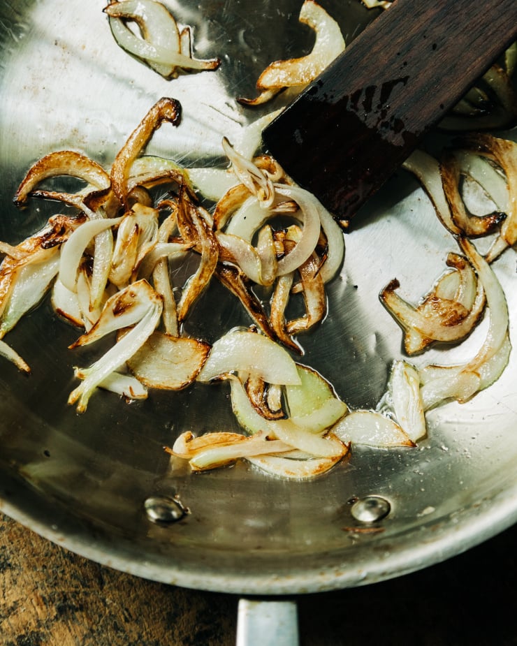 An overhead image shows caramelized slices of onion in a stainless steel sauté pan.