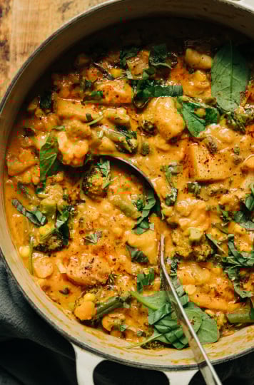 An up close overhead shot of a light orange creamy vegetable stew that features sun dried tomatoes, baby spinach, and garlic.
