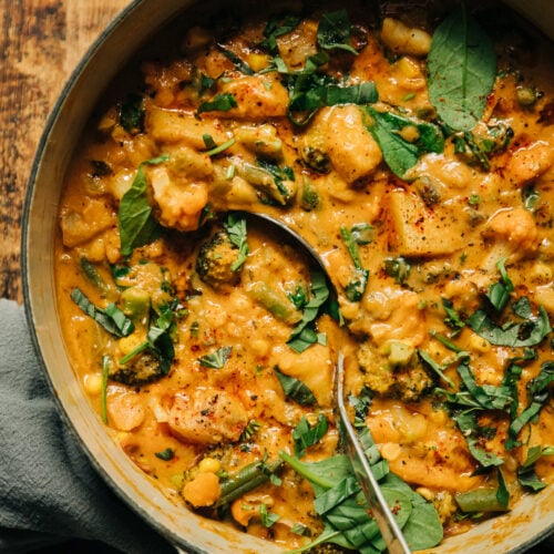 An up close overhead shot of a light orange creamy vegetable stew that features sun dried tomatoes, baby spinach, and garlic.