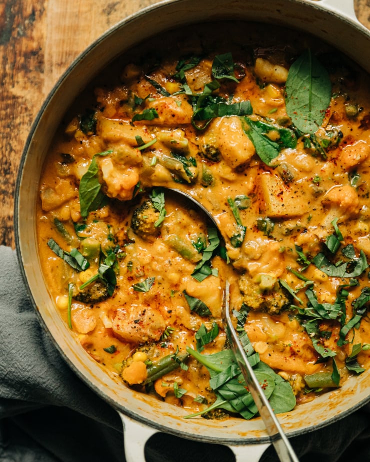 An up close overhead shot of a light orange creamy vegetable stew that features sun dried tomatoes, baby spinach, and garlic.