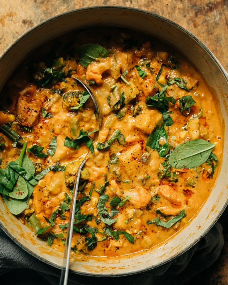 An up close overhead shot of a light orange creamy vegan vegetable stew that features sun dried tomatoes, baby spinach, and garlic.