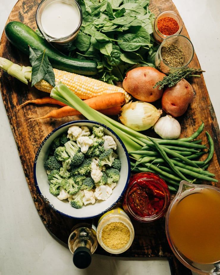 An overhead shot shows ingredients used in a creamy vegan vegetable stew recipe on top of a rustic wooden cutting board.