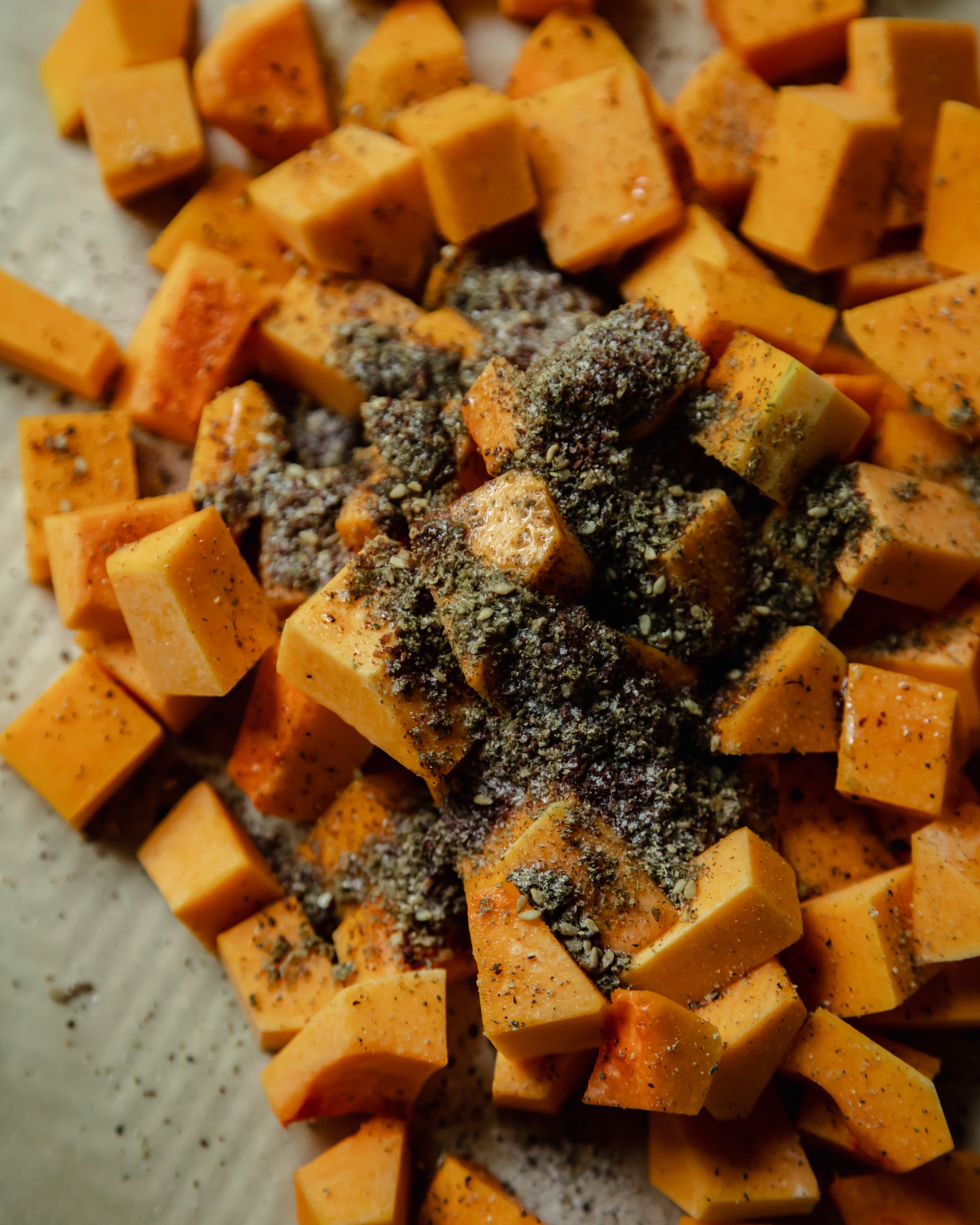 An up close, overhead shot of a pile of cut butternut squash with a lot of za'atar on top.