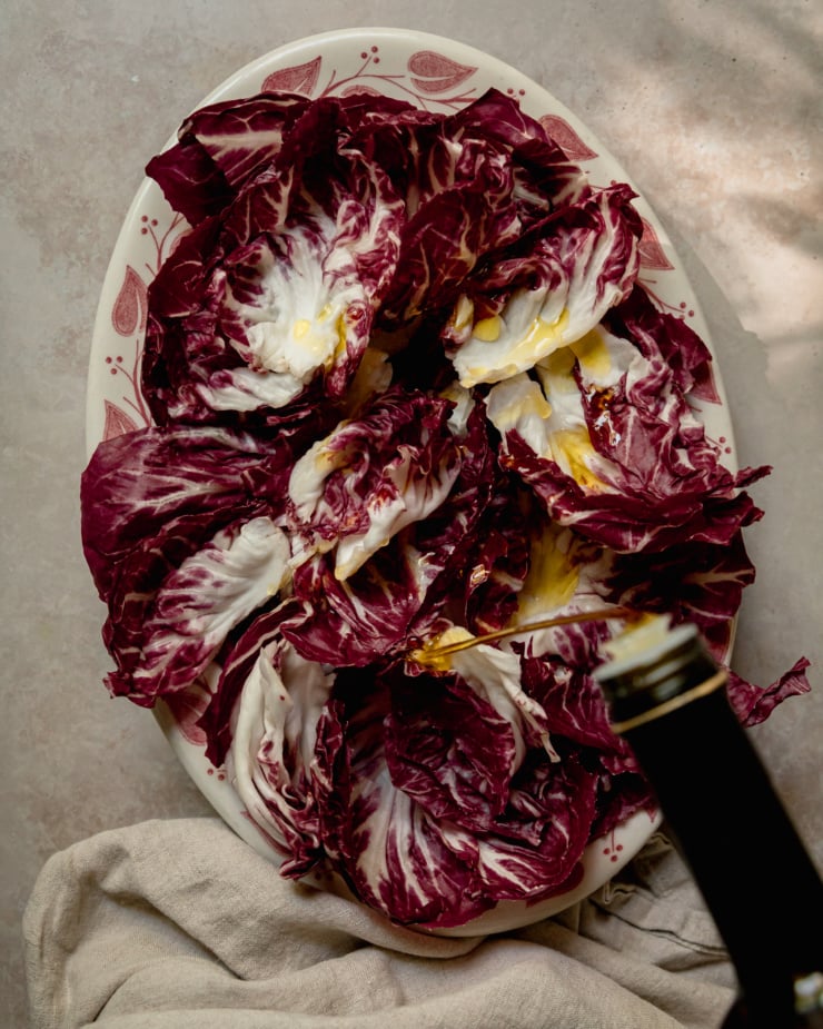 An overhead shot shows a platter of radicchio leaves being drizzled with olive oil.