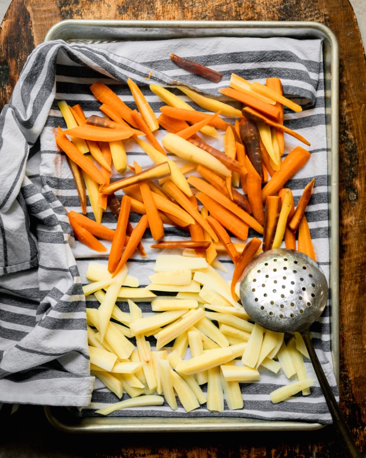 An overhead shot of boiled cut carrots being dried over a blue striped kitchen towel set inside of a baking sheet.