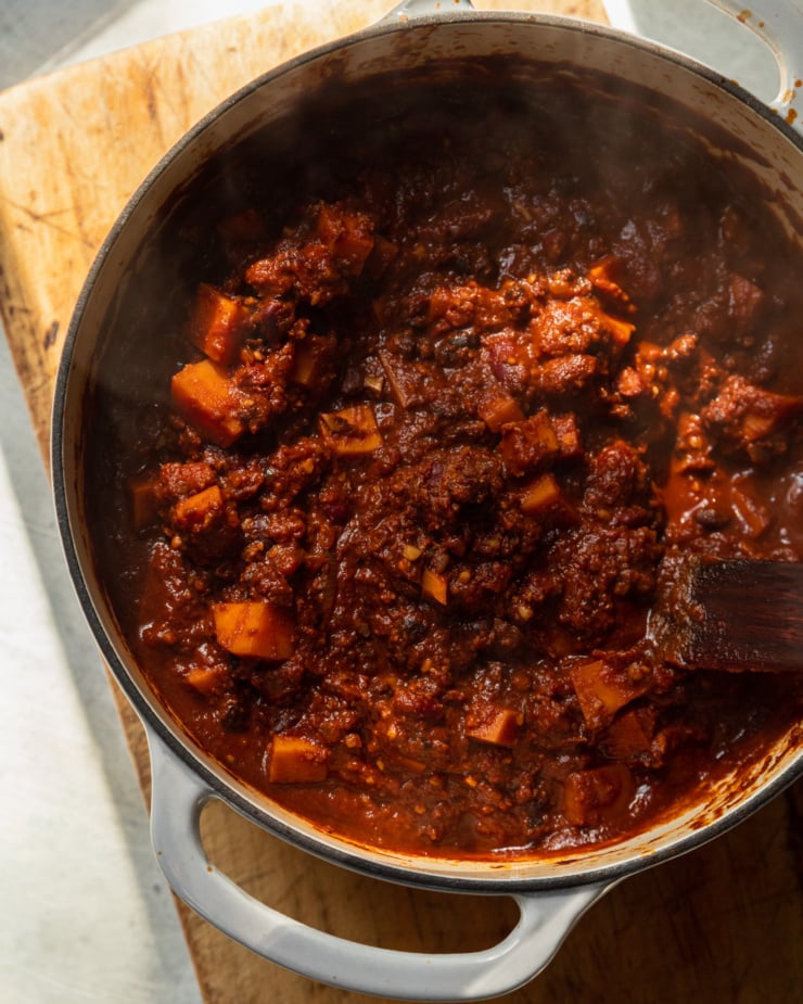 An overhead shot shows a Dutch oven filled with a steaming pot of vegan sweet potato walnut chili.