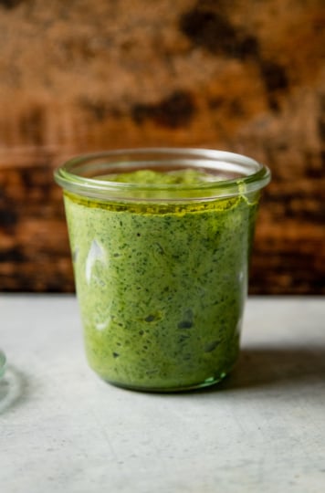 A head-on shot of a glass jar filled with vegan pesto.