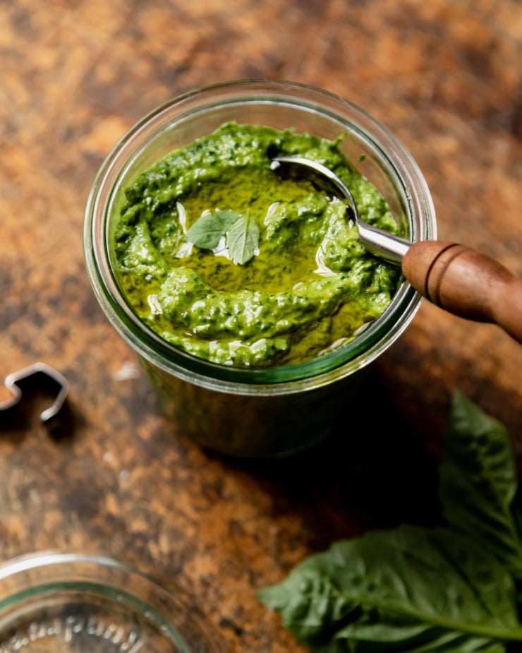 A slight 3/4 angle shot shows a jar of vegan pesto with a spoon sticking out of the jar.