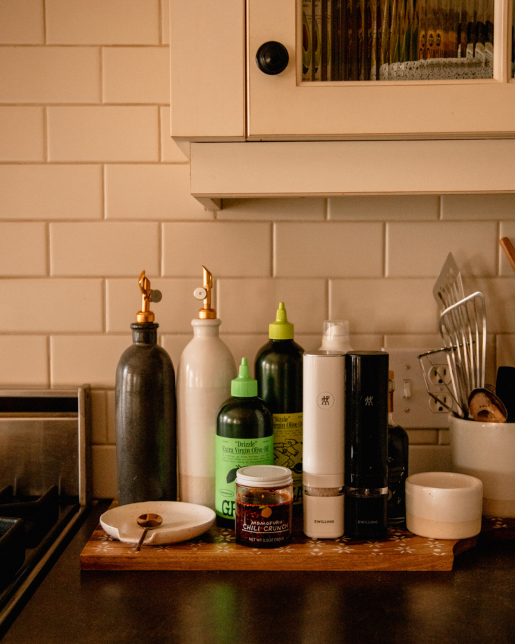 A head on shot of ingredients by a stove: different bottles of olive oil, salt and pper grinders, chili oil, and spices.