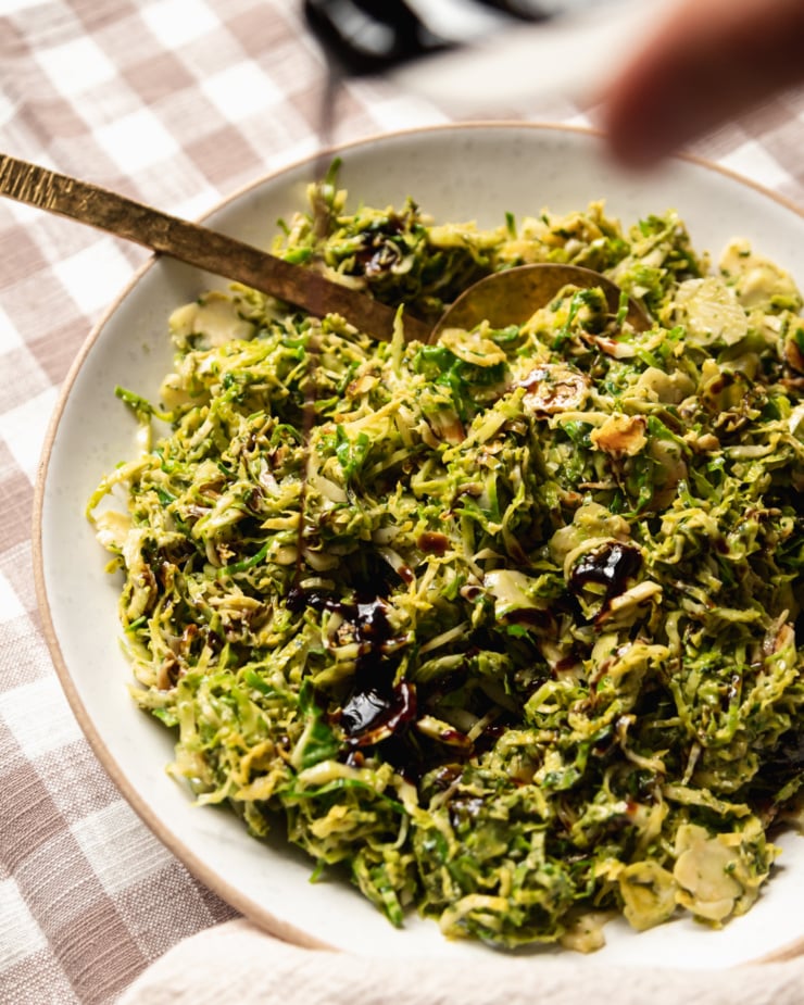 A 3/4 angle shot of balsamic glaze being poured over cooked and sliced brussels sprouts.