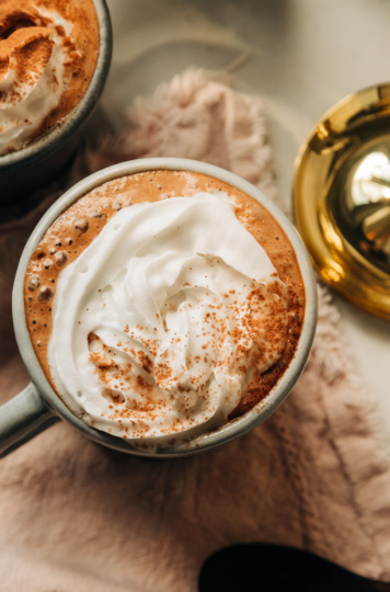 An overhead shot of vegan almond butter hot chocolate in a mug, topped with a swirl of coconut whipped cream and a sprinkle of cocoa powder.