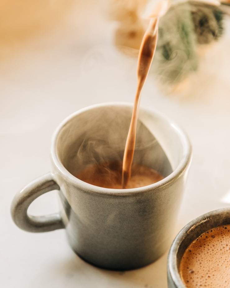 A 3/4 angle image shows hot chocolate being poured into a mug. Steam is pouring out.