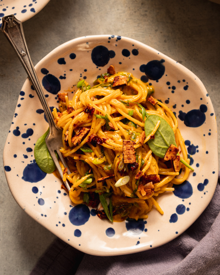 An overhead shot shows a serving of butternut squash coconut milk noodles in a shallow bowl. A fork is sticking out to the side.