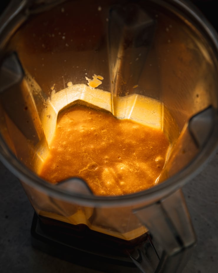 A 3/4 angle shot shows a blender pitcher with puréed butternut squash sauce, backlit by a beam of sunlight.