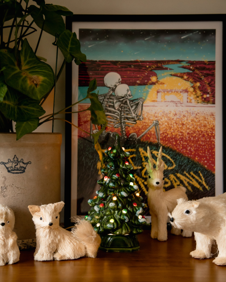 A head on shot of a ceramic Christmas tree decoration that is all lit up. On each side are ornamental Winter animal decorations and a large ivy plant.