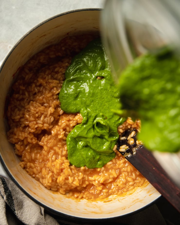 An overhead shot of a deep greenbroccoli rabe purée being added to a pot of fully cooked risotto.