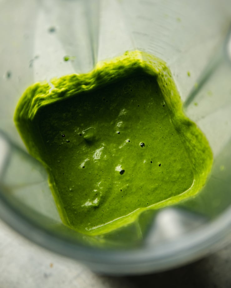 An up close overhead shot into a blender showing a deep green purée of broccoli rabe, green onions, and olive oil.